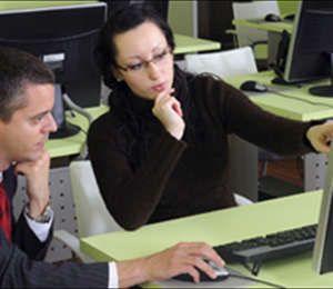 A woman and a man engaged in discussion while looking at a computer screen.